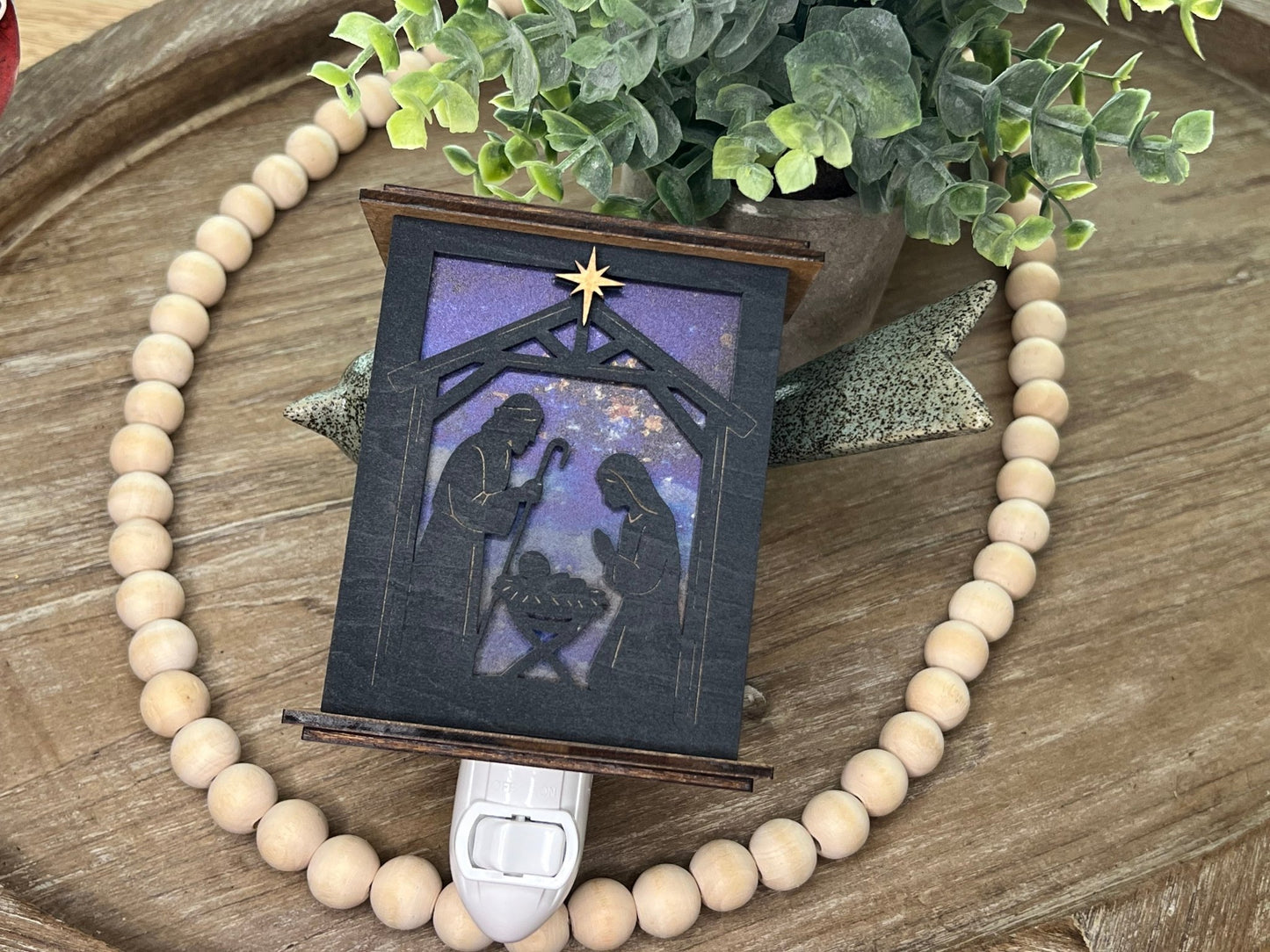 Rustic nativity nightlight lantern made of black wood and golden oak stained acrylic lynig down with front view and unlit.