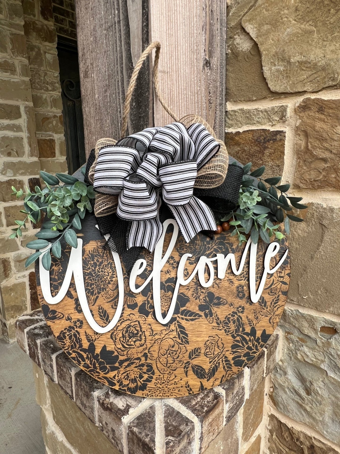 Wooden butterfly door hanger with floral design in natural wood and black accents leaning against wood post..