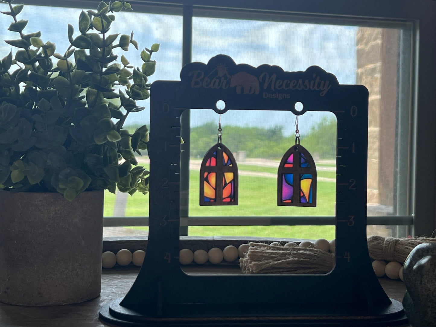 Arched window stained glass effect earrings made of wood and acrylic, showcasing a colorful and rustic design in sunlight.
