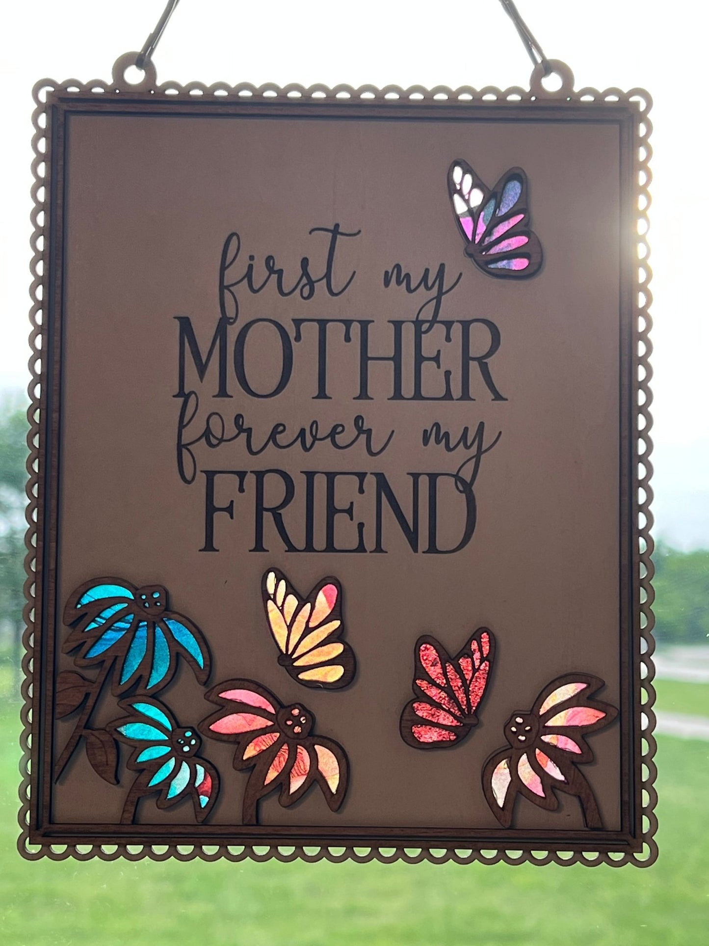Colorful Mother Butterfly Suncatcher made of acrylic and wood, hanging in a window in sunshine.